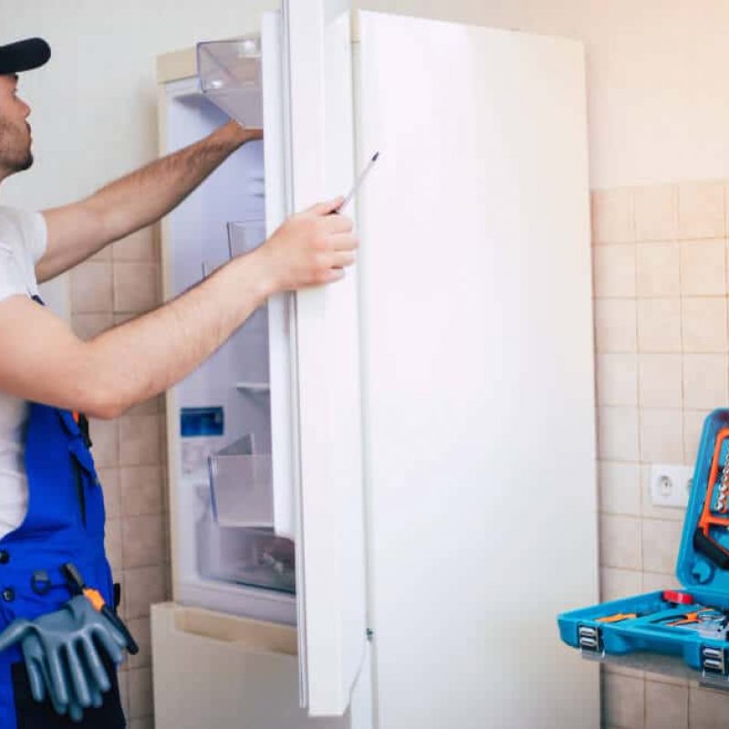 professional-young-repairman-worker-uniform-cap-with-modern-toolbox-with-equipment-is-repairing-refrigerator-kitchen (1)
